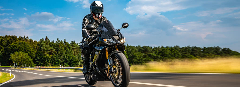 Person wearing black motorcycle gear and helmet riding a black sport motorcycle - www.compassinsurancegroup.com