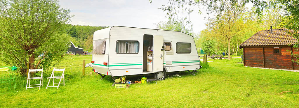 White camper trailer with green stripes parked on a grassy field near trees - www.compassinsurancegroup.com
