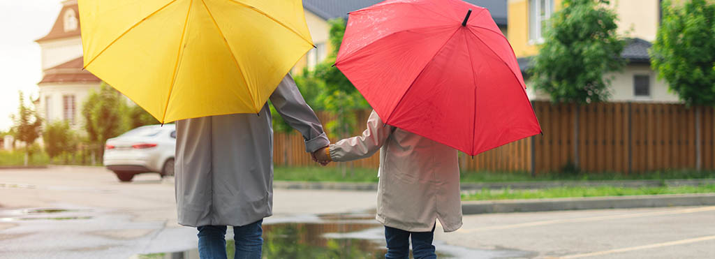 Two people holding hands walking on a wet street - www.compassinsurancegroup.com